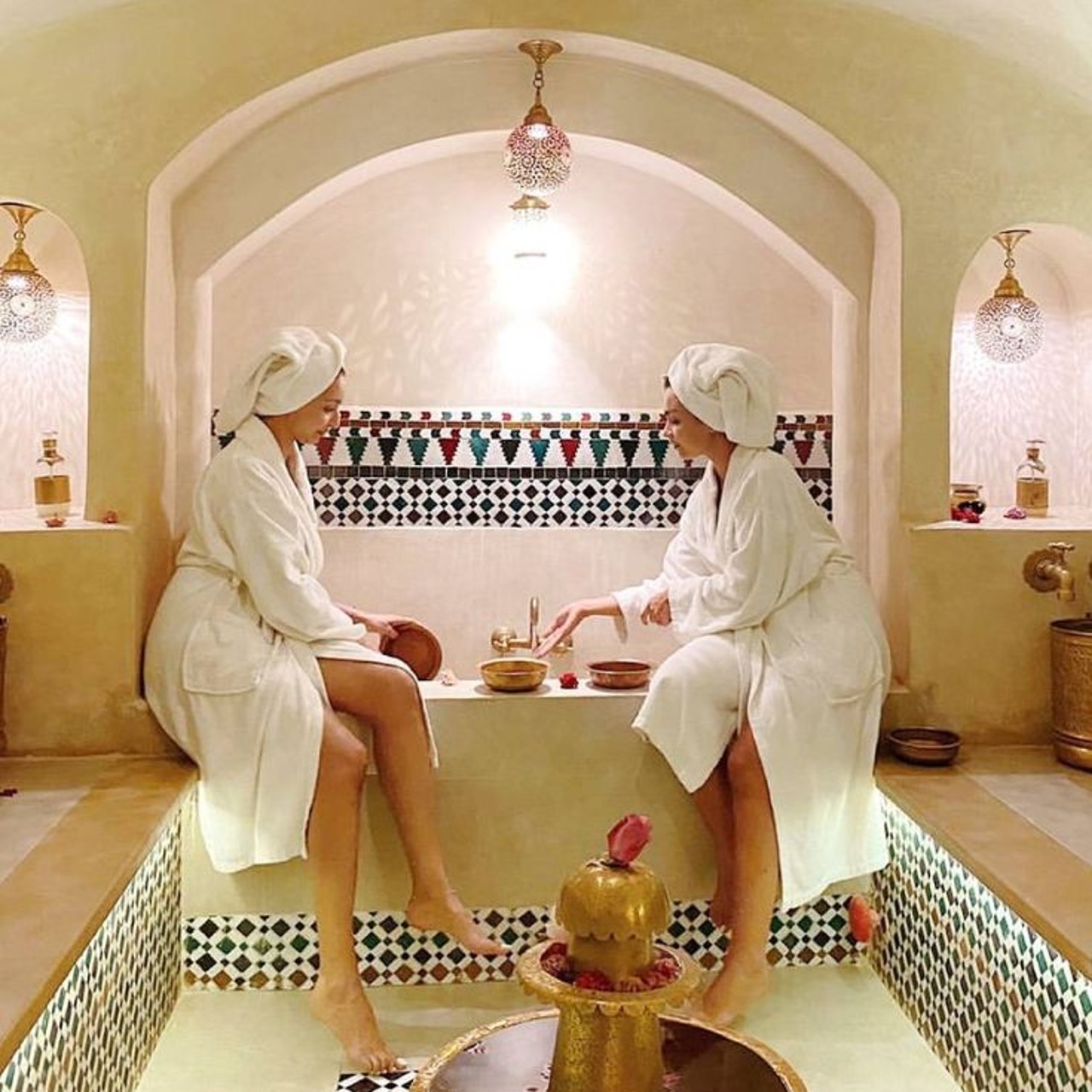 Two guests in robes inside a traditional Marrakech hammam with carved plaster walls